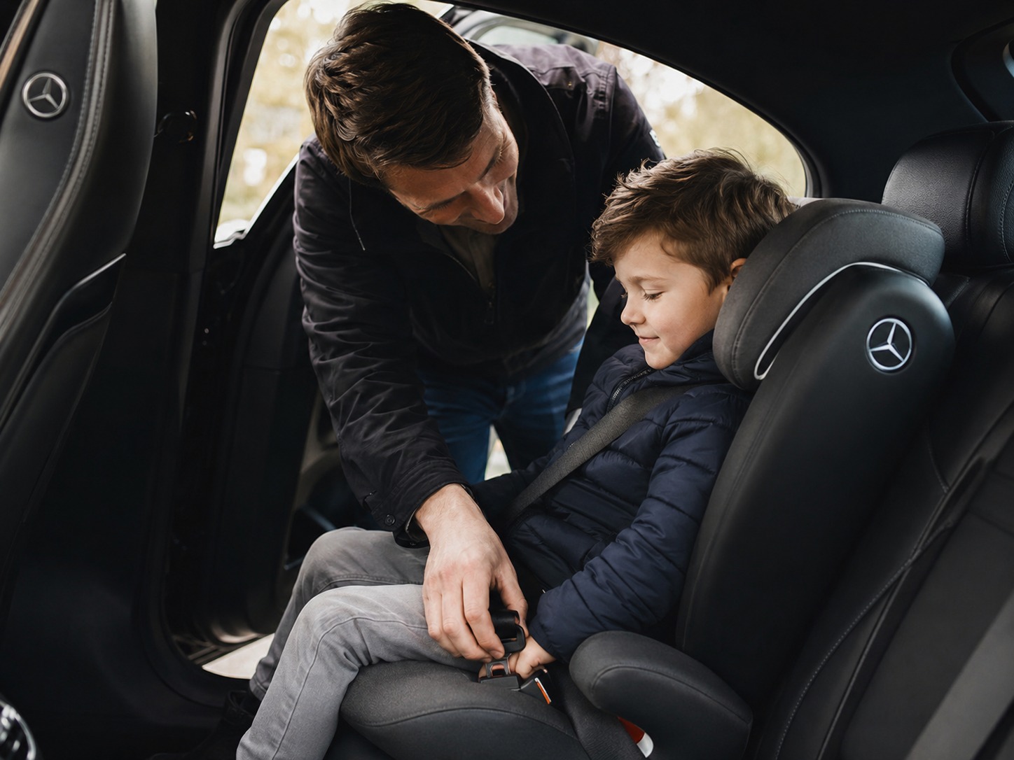 Parent securing a young child into a fitted child seat in the back of a clean saloon taxi